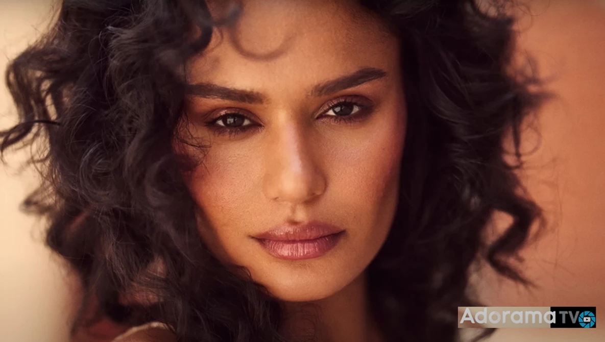 Woman with wavy dark hair and warm, neutral makeup looking directly at camera with soft expression.