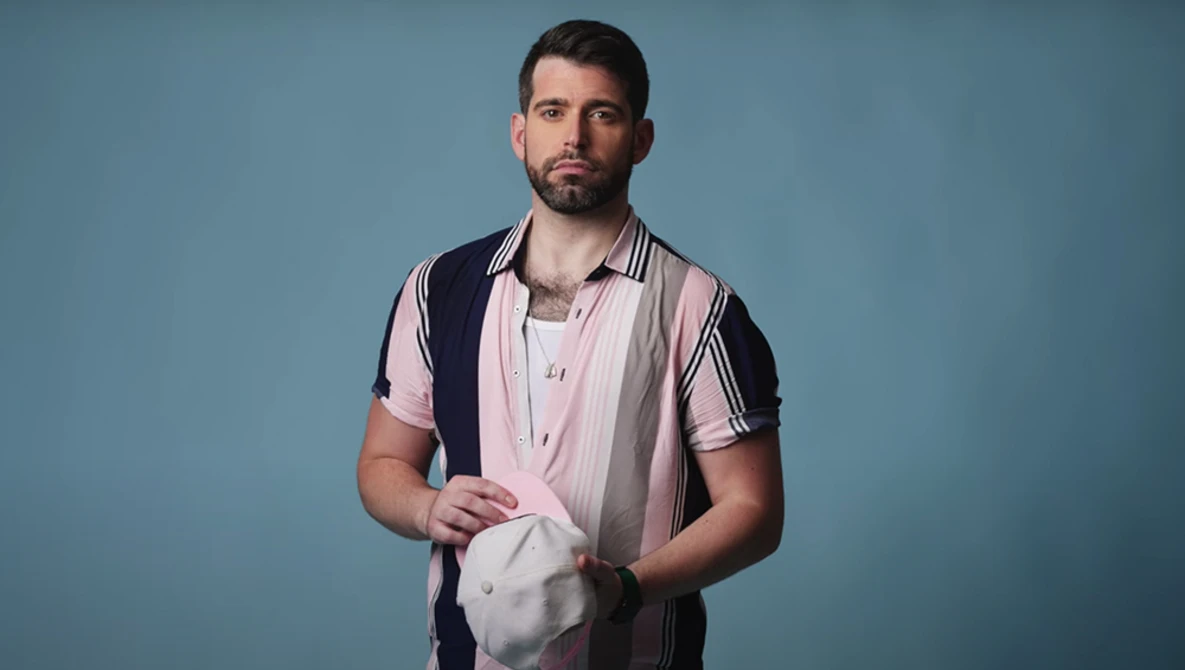 Man in pink and black striped shirt holding white fabric against blue background.