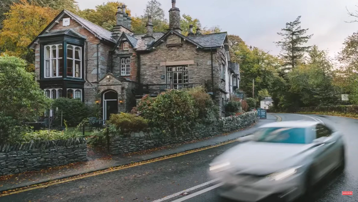 Stone mansion with bay windows beside a blurred moving car on a rural road.