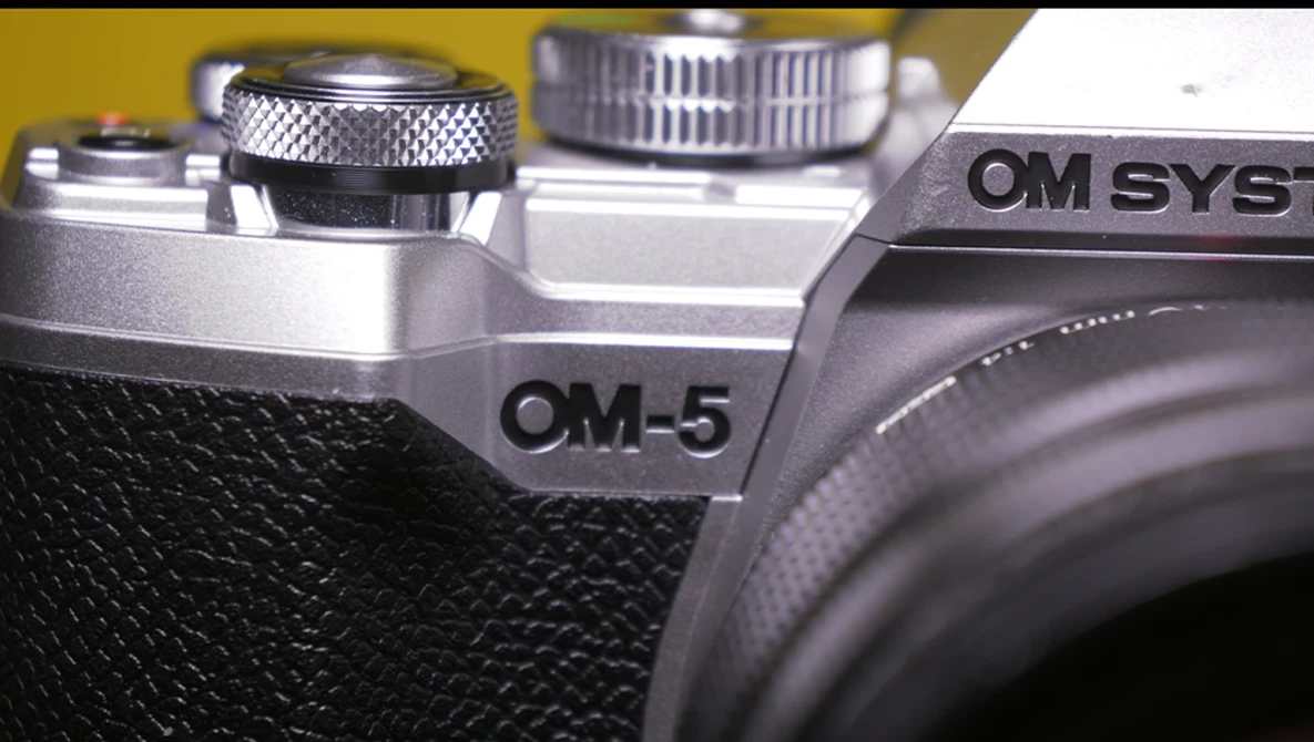 Close-up detail of OM-5 and OM SYS camera bodies showing textured grip and control dials.