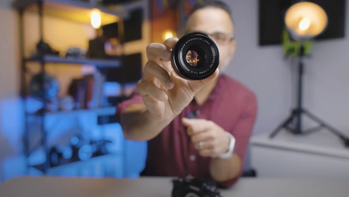 Photographer holding a vintage camera lens toward the camera in a studio environment.