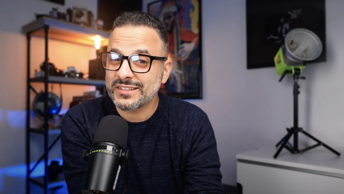 Man wearing glasses and black shirt speaking into a professional microphone in a studio setting.