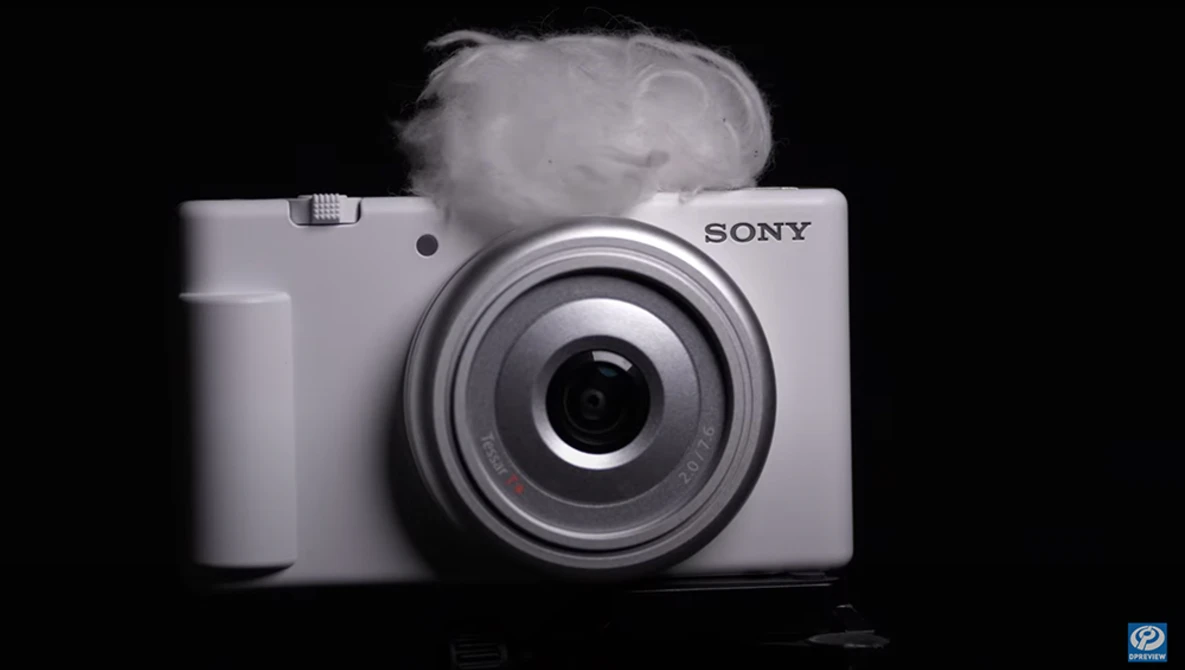 White Sony compact camera with circular lens on black background with atmospheric smoke effect.