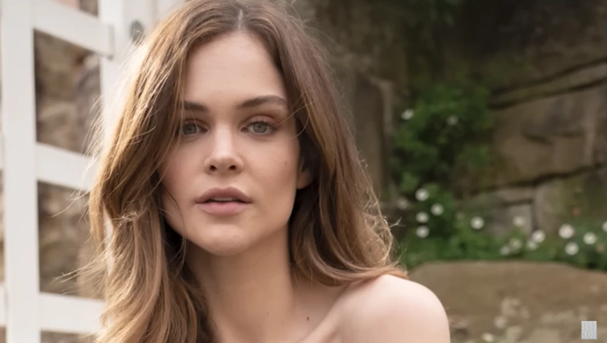 Woman with shoulder-length brown hair looking directly at camera in outdoor garden setting.