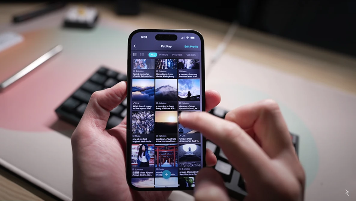 Hands holding a smartphone displaying a grid of thumbnail images and video content.