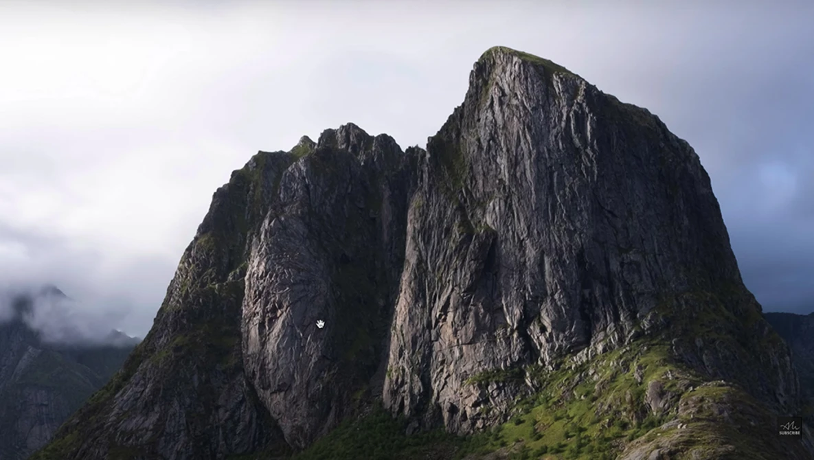 Two dramatic dark rock peaks with vertical columnar formations rising above green alpine slopes under overcast sky.