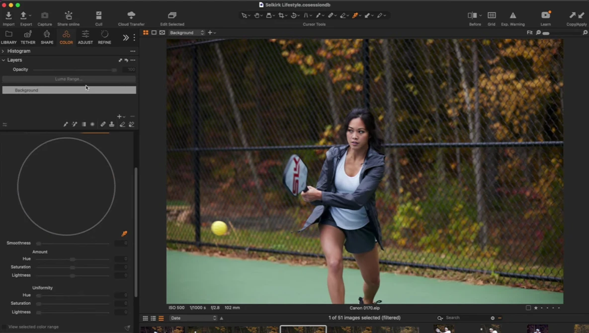 Female tennis player in mid-swing on outdoor court during golden hour, with chain-link fence and autumn foliage in background.