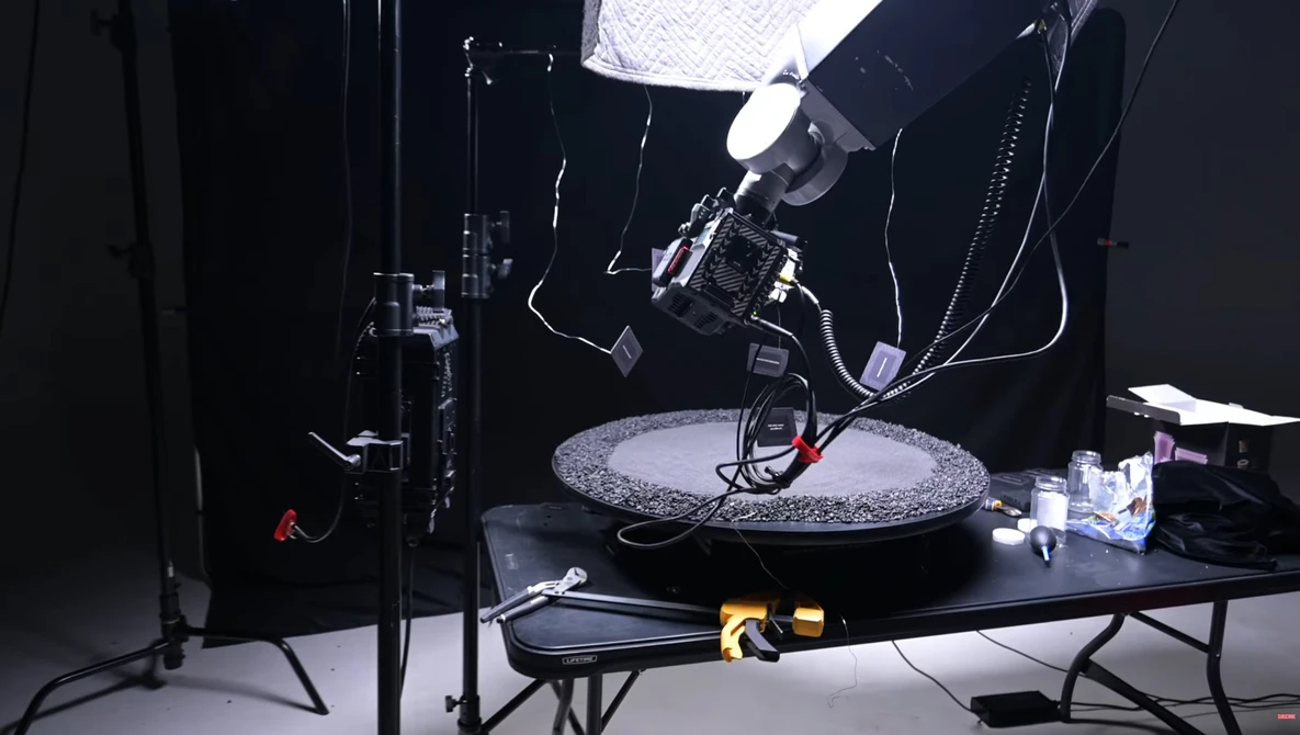 Professional overhead lighting setup with softbox and key light positioned above a circular reflective surface on a dark studio table.