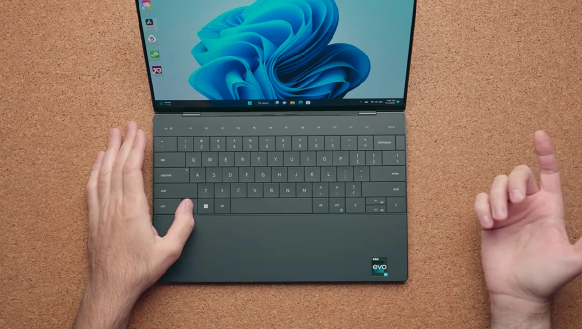 Hands positioning a laptop with Windows 11 startup screen on cork surface.