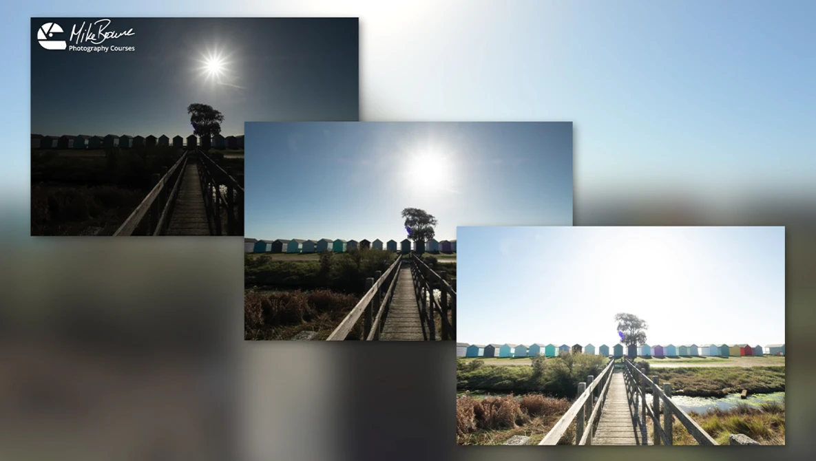 Wooden boardwalk stretching into a landscape with moored boats and fields under bright sunlight.