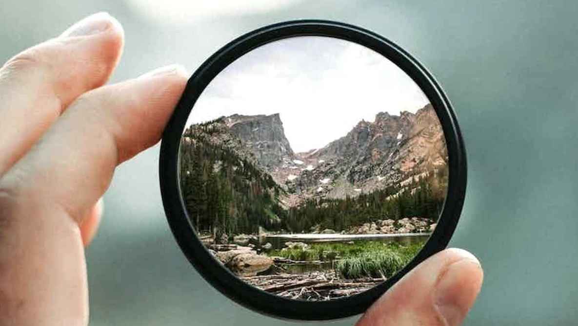 Mountain valley landscape framed through a circular lens filter held in hand.