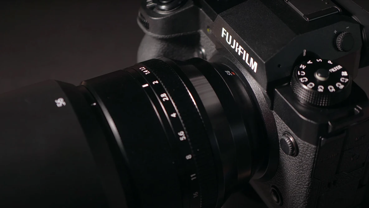 Fujifilm camera with attached lens against dark background, showing camera body and control dial.