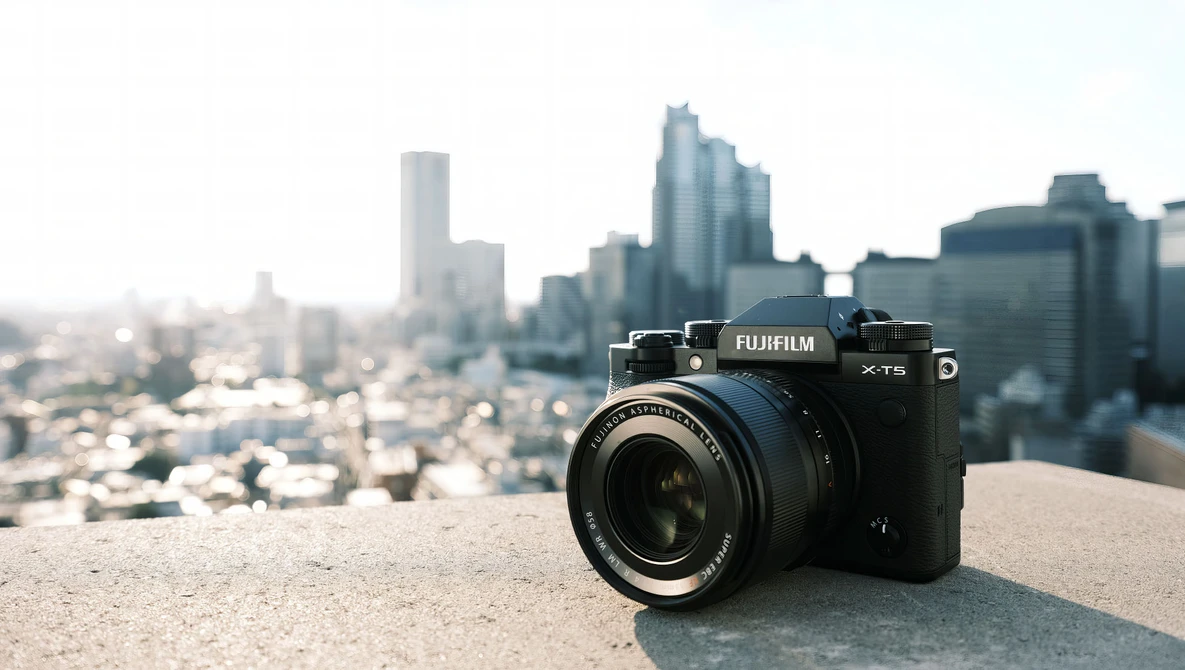 Fujifilm X-T5 camera on concrete ledge with blurred city skyline behind.
