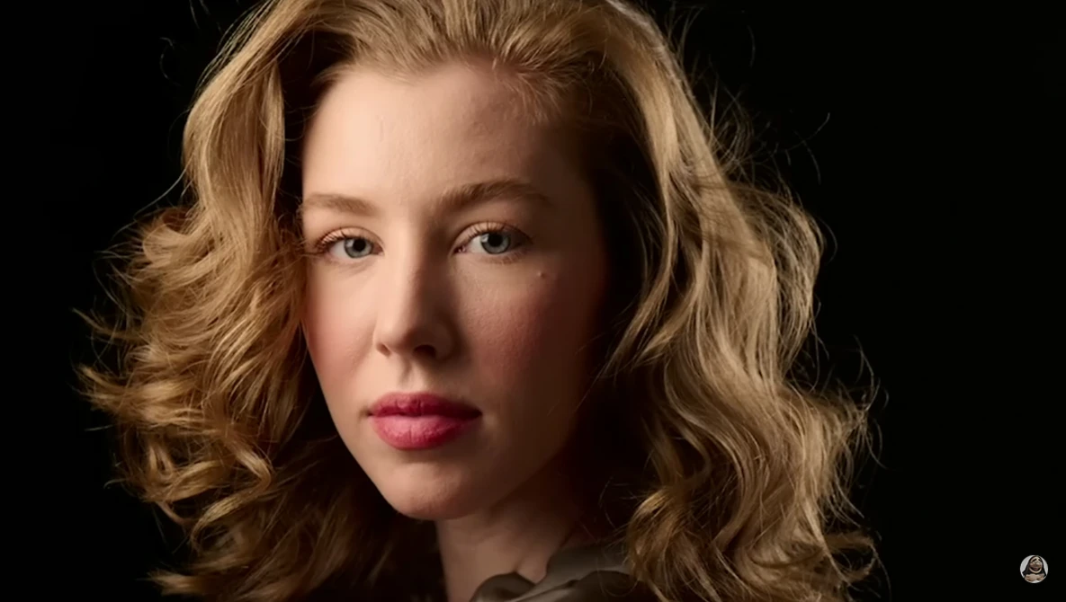 Woman with wavy blonde hair and pink lipstick against a black background.