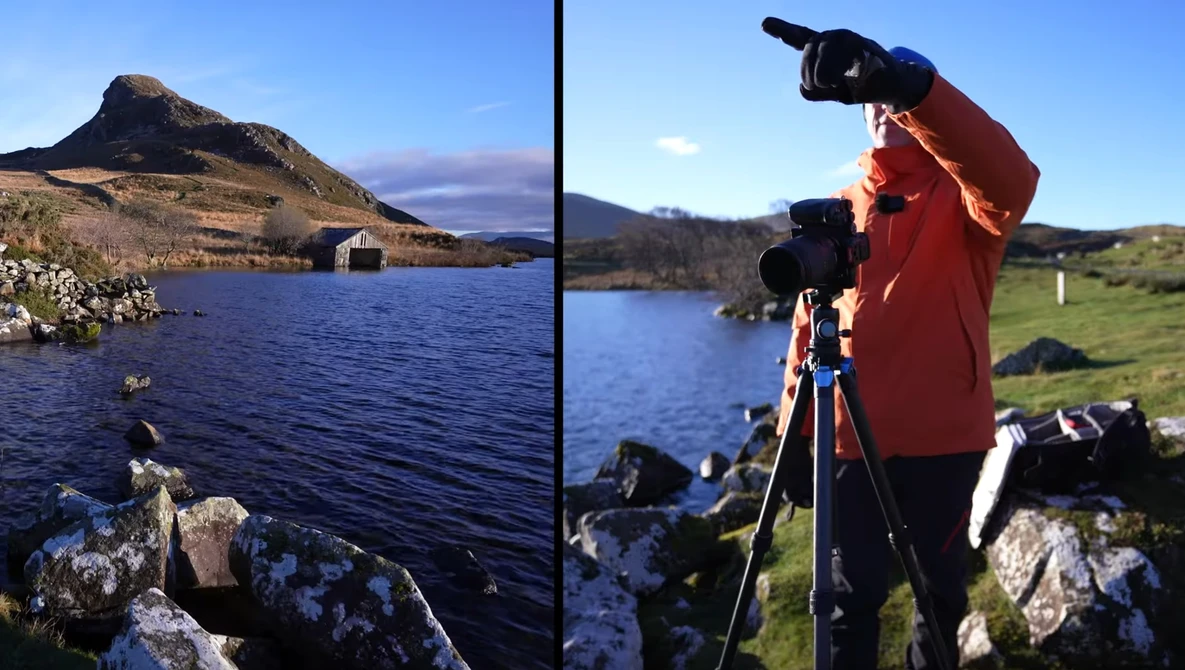 Photographer operating a camera on tripod while framing a mountain landscape with lake below.