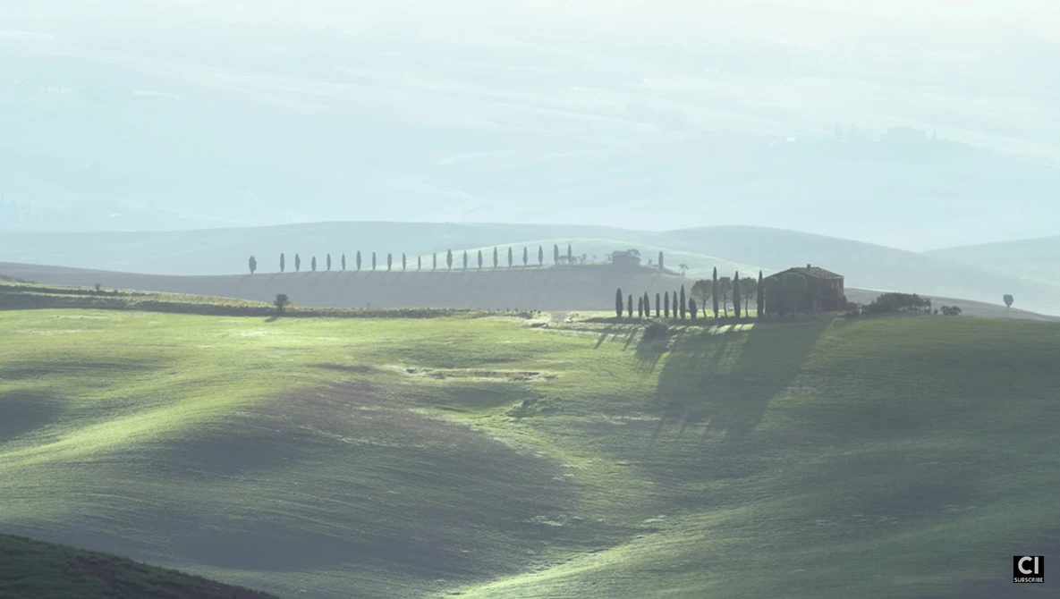 Tuscan villa with cypress trees on rolling hillside at golden hour, dramatic shadows across plowed fields.