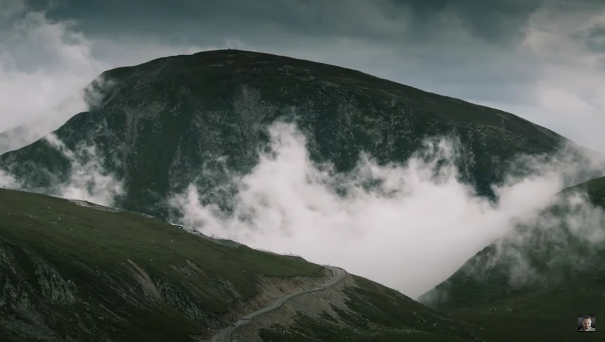 A verdant mountain peak shrouded in mist and low-hanging clouds beneath a dramatic overcast sky.