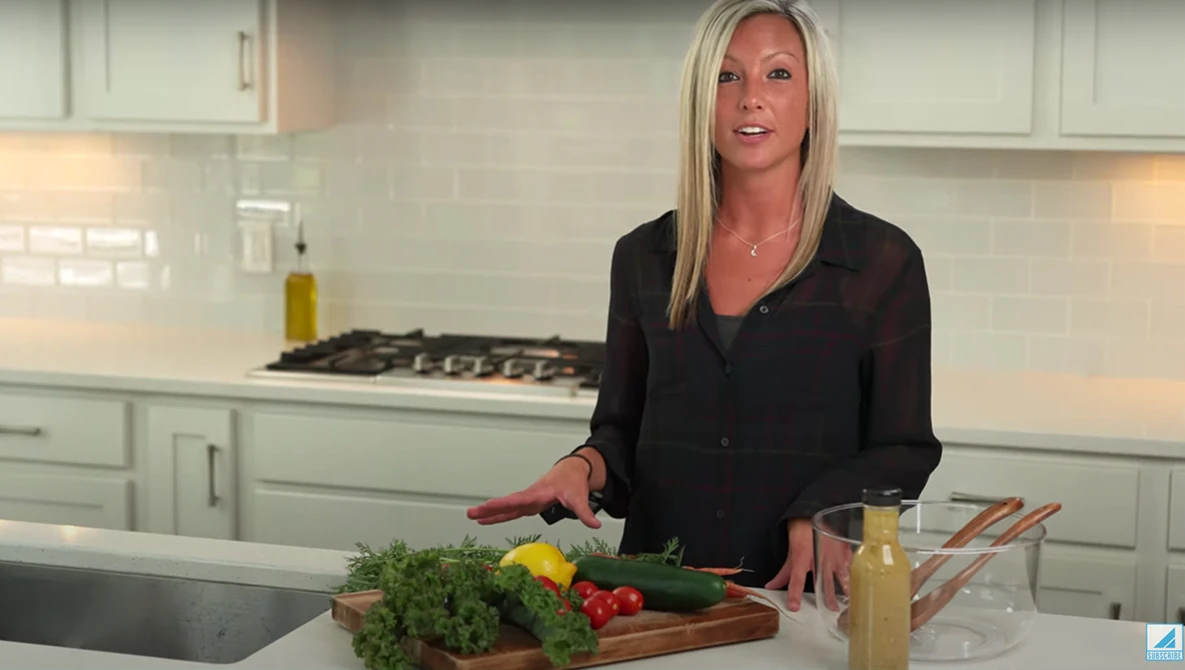 Woman in black blazer preparing fresh vegetables at a kitchen counter with professional lighting.