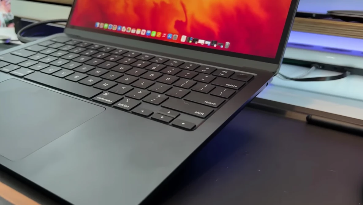 MacBook laptop displaying warm red and orange wallpaper with dock visible at screen top.