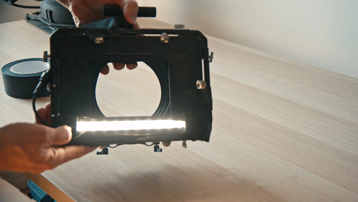 Photographer's hands holding an open matte box with a circular opening and light diffusion panel.