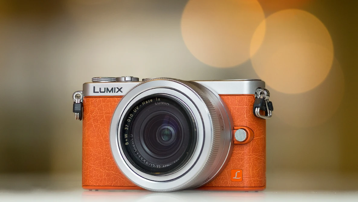 Panasonic Lumix GM1 mirrorless camera with orange leather body and silver trim, featuring a standard zoom lens.