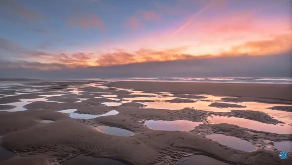Aerial view of tidal flats and shallow pools at sunset with pink and orange sky.
