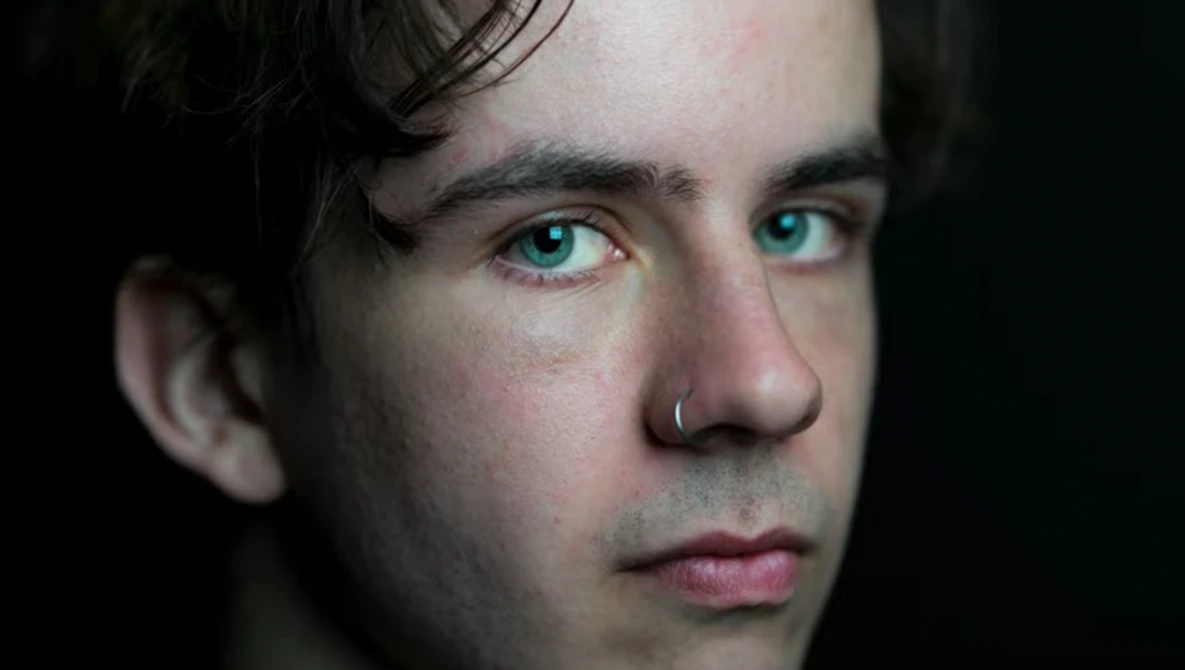 Close-up portrait of a person with striking teal eyes against a dark background.