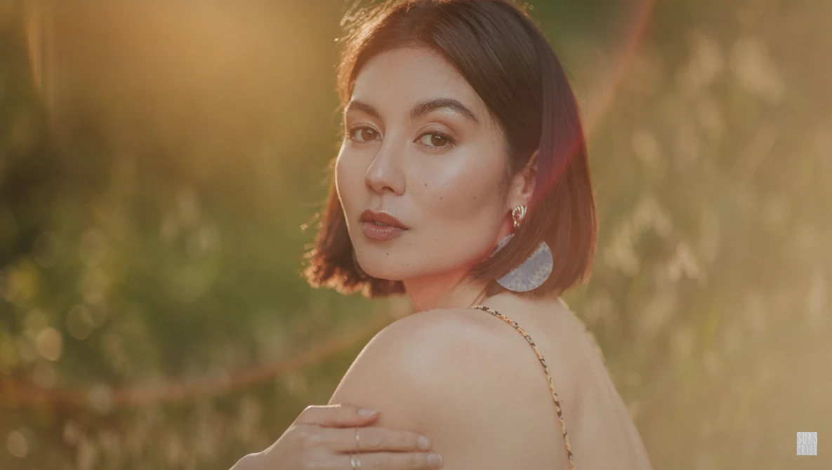 Woman with short reddish-brown hair looking over her shoulder in warm, golden hour lighting.