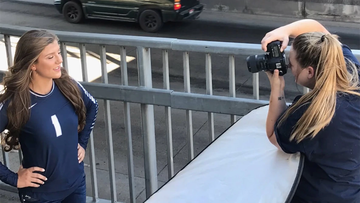 Photographer holding camera to face while shooting a subject in navy athletic wear on an urban overpass.