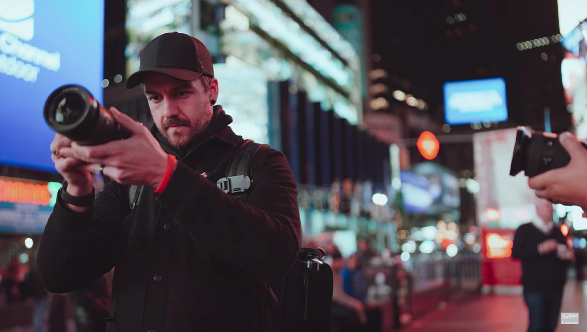 Photographer holding a camera with telephoto lens on a busy city street at night.