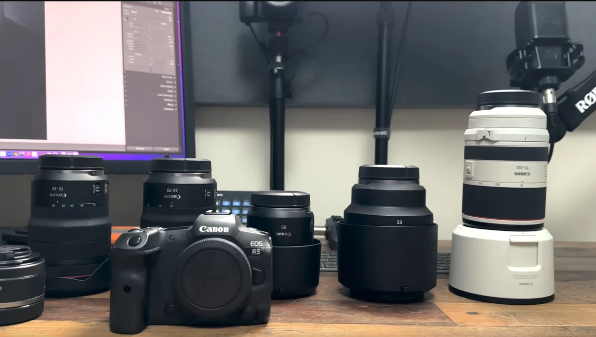 Canon DSLR camera body surrounded by various lenses on a wooden surface.