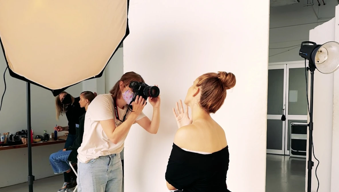 Photographer shooting a portrait of a woman against a white backdrop in a studio setting.