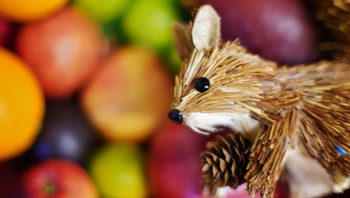 Handcrafted wooden deer ornament with natural fiber details against a blurred background of colorful fruit.