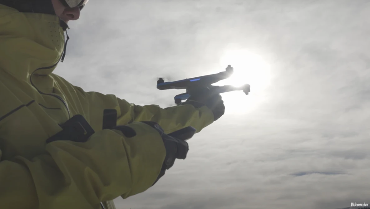 Person in yellow jacket holding a quadcopter drone against overcast sky.