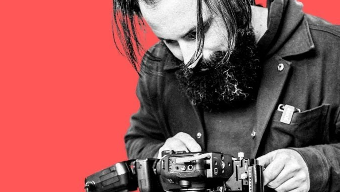Photographer holding a film camera against a bright red background.
