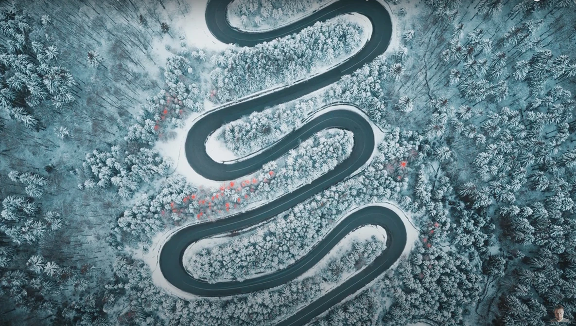Aerial view of a winding mountain road cutting through snow-covered forest.
