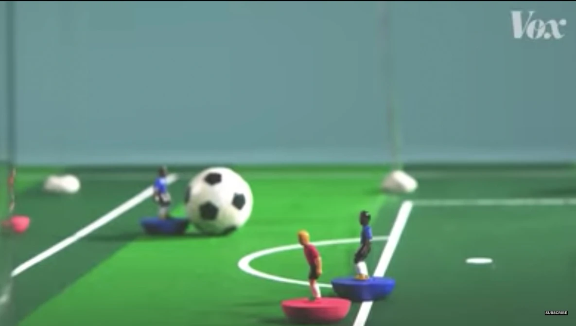 Illustration of a miniature soccer field with figurine players and a ball.