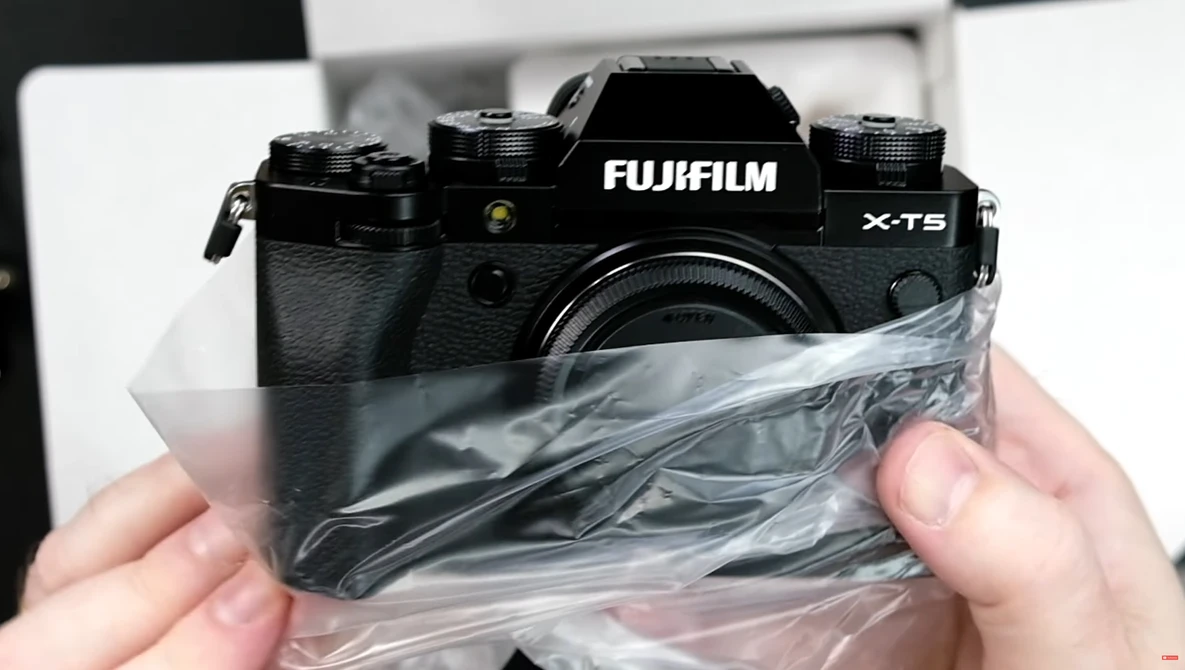 Fujifilm X-T5 camera held in hands with plastic protective wrapping partially removed.