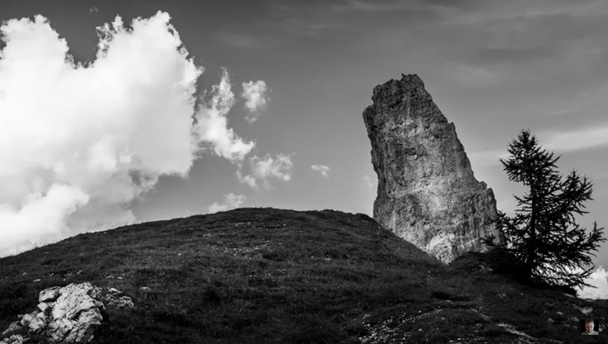 Dramatic rocky pinnacle rising from a forested hillside beneath cloudy sky.