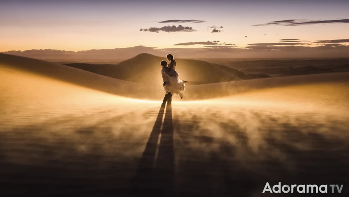 Silhouetted figure standing on desert sand dunes during golden hour sunset with dramatic atmospheric dust clouds.
