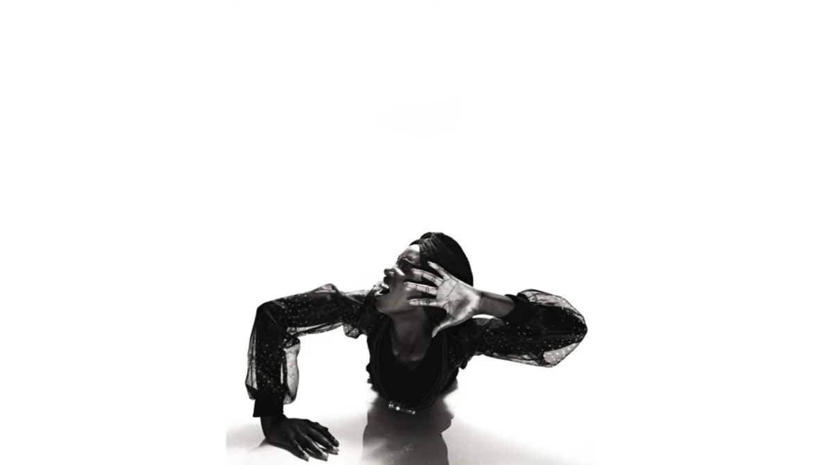 High-contrast black and white studio portrait of a shirtless man in a dramatic crouching pose against a white background.