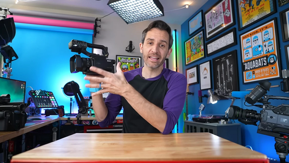 Content creator holding a compact video camera in a colorful studio setup with blue walls and professional lighting.