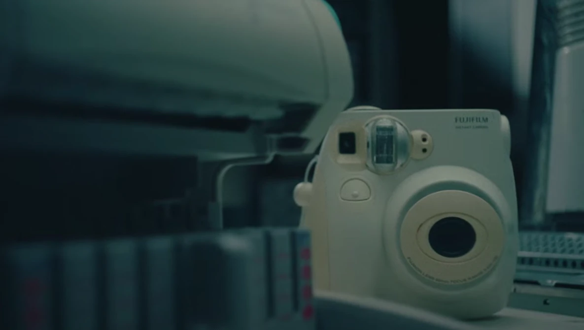 White Fujifilm Instax Mini instant camera displayed on a desk beside a laptop keyboard.