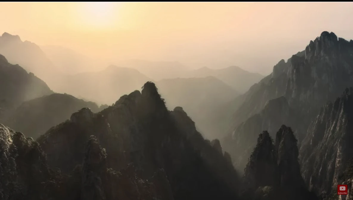 Misty mountain valley at sunrise with layered peaks silhouetted against golden light.