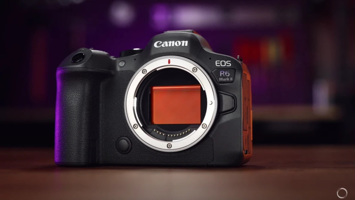 Canon EOS R5 Mark II mirrorless camera with lens mount exposed, displayed against blurred purple and warm-toned background.