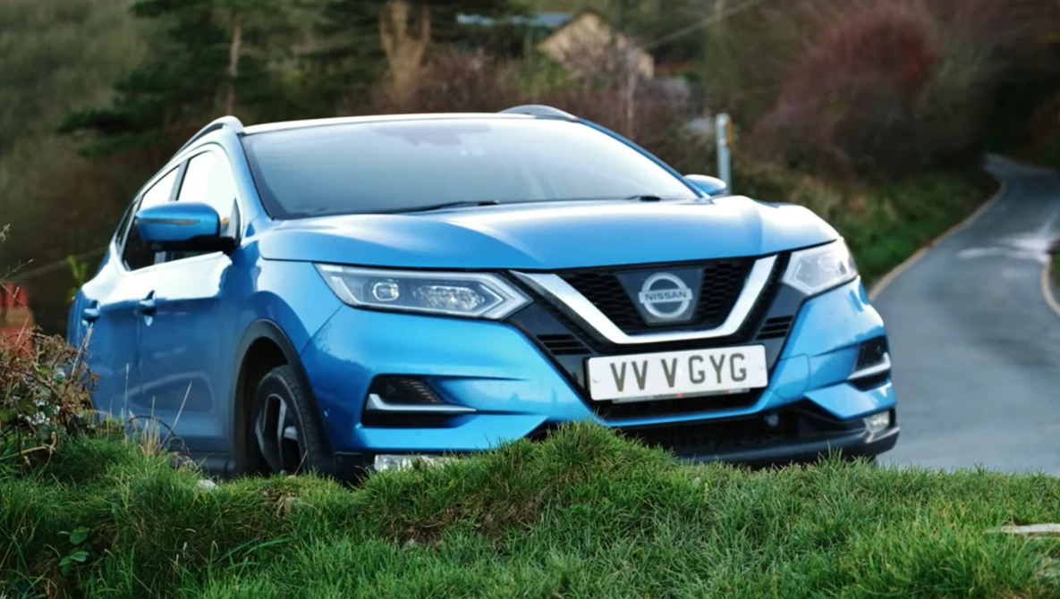 Blue Nissan compact SUV parked on grass with trees in the background.