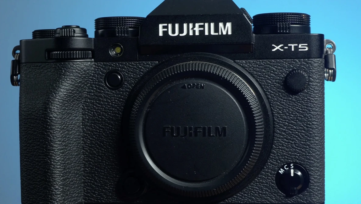 Fujifilm X-T5 mirrorless camera body against a blue gradient background.