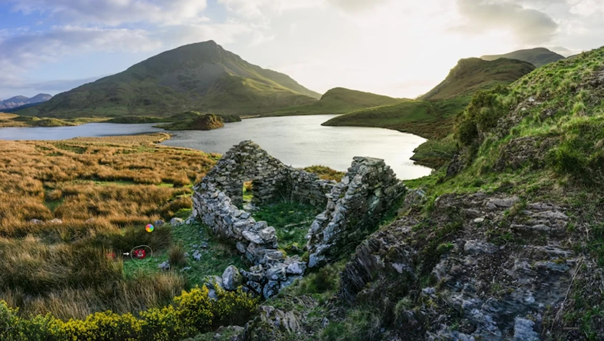Glacial lake surrounded by moss-covered lava rock formations and green mountainous terrain under partly cloudy sky.
