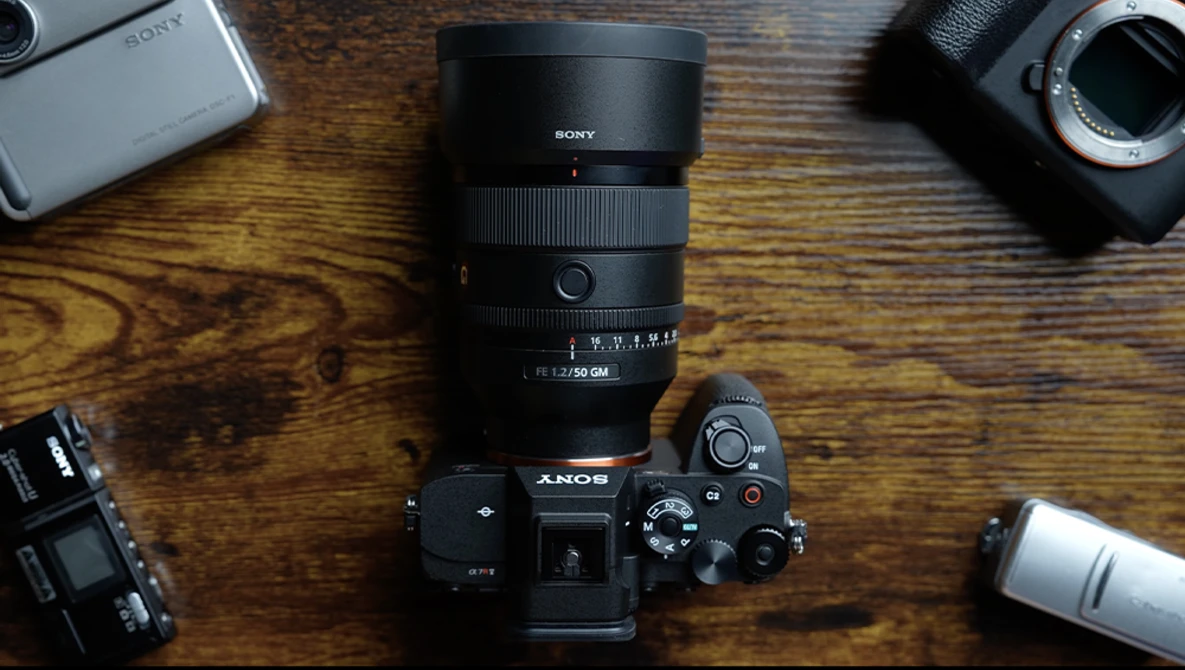 Sony camera body with attached telephoto lens surrounded by additional lenses and camera equipment on wooden surface.