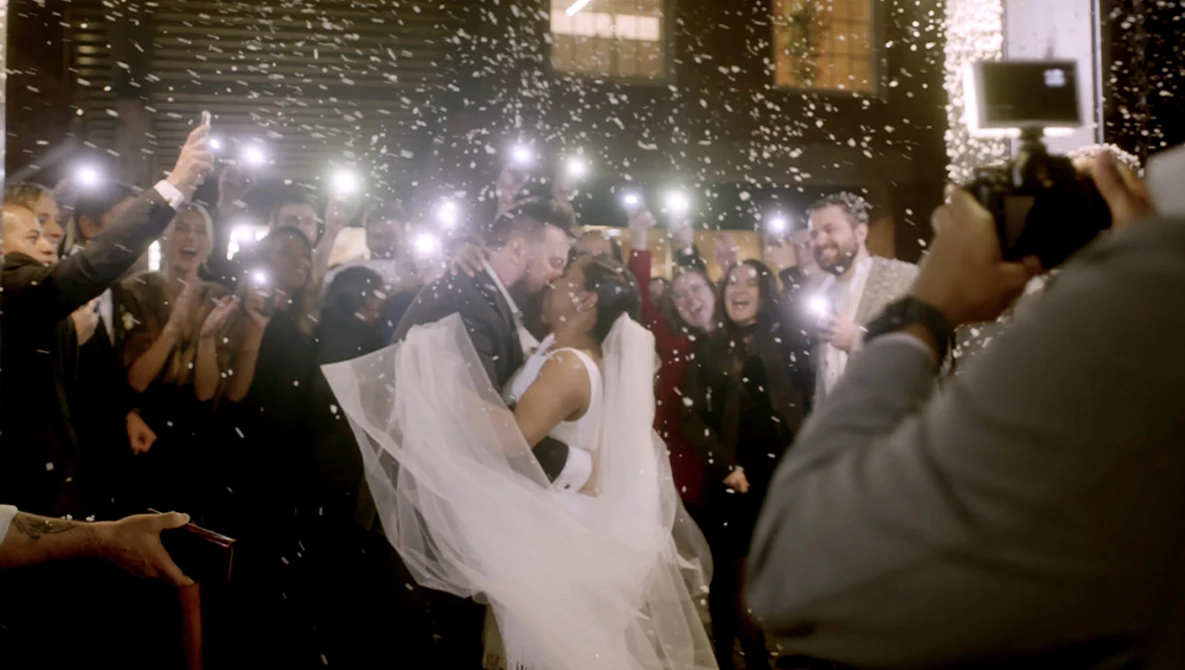 Bride and groom dancing while surrounded by guests holding up illuminated phones and cameras.